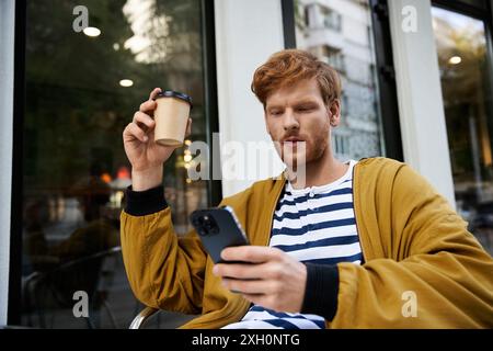 Jeune homme aux cheveux roux en tenue debonair assis à l'extérieur, engrossé dans un téléphone portable. Banque D'Images