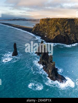 Vue aérienne des piles marines de Reynisdrangar le long de la côte sud de l'Islande, avec des falaises spectaculaires et des vagues océaniques. Banque D'Images