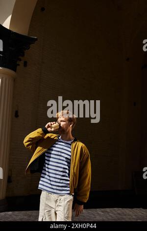 Jeune homme aux cheveux roux en tenue de débonair buvant du café à l'extérieur du bâtiment. Banque D'Images