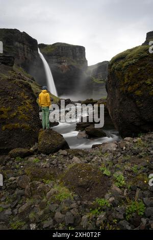 Jeune homme avec une veste jaune debout devant la cascade, Haifoss et Granni cascade à un canyon, Fossa i Pjorsardal, avec la rivière i. Banque D'Images