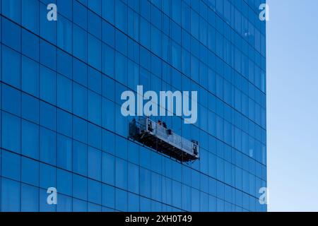 Buffalo, New York, États-Unis - 8 décembre 2023 : deux nettoyeurs de vitres dans une plate-forme suspendue nettoyant le mur-rideau en verre d'un immeuble de bureaux de grande hauteur Banque D'Images