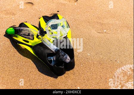 Équipement de plongée en apnée sur le sable avec les vagues de l'océan éclaboussant l'eau. Nageoires noires, masque noir, tuba sur fond de texture sablonneuse. Objets se trouvant dans Banque D'Images