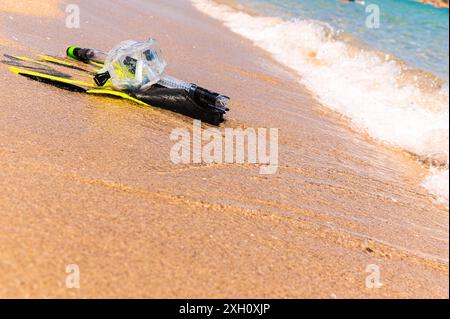 Équipement de plongée en apnée sur le sable avec les vagues de l'océan éclaboussant l'eau. Nageoires noires, masque noir, tuba sur fond de texture sablonneuse. Objets se trouvant dans Banque D'Images