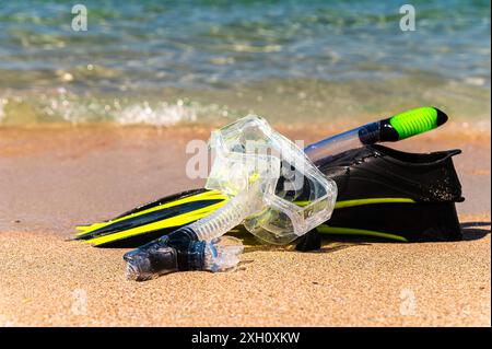 Équipement de plongée en apnée sur le sable avec les vagues de l'océan éclaboussant l'eau. Nageoires noires, masque noir, tuba sur fond de texture sablonneuse. Objets se trouvant dans Banque D'Images