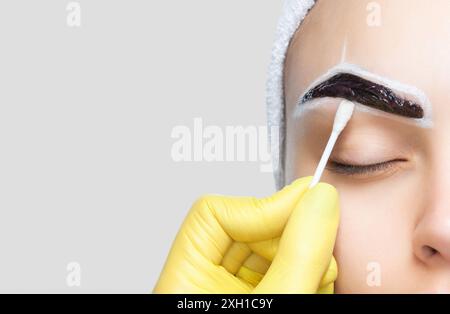 Le maquilleur essuie la peinture au henné des sourcils de la fille. La procédure de teinture des sourcils avec de la peinture dans le salon de beauté. Banque D'Images