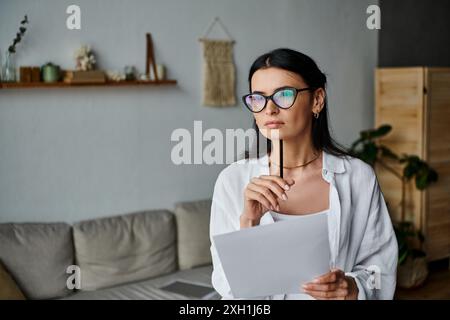 Femme avec des lunettes travaillant à la maison tient du papier Banque D'Images