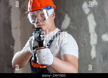 Le constructeur avec l'équipement de perforateur de perceuse à percussion faisant le trou dans le mur sur le chantier de construction. Travaux de réparation, décoration intérieure des murs. Banque D'Images