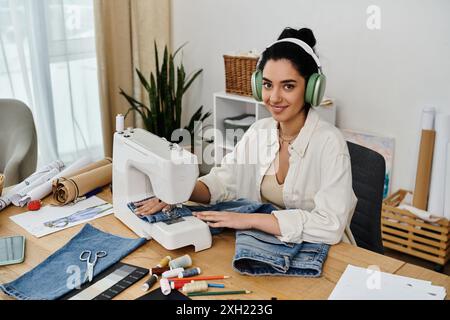 Une jeune femme en tenue décontractée s'assoit à un bureau, machine à coudre en action tout en upcycling vêtements. Banque D'Images