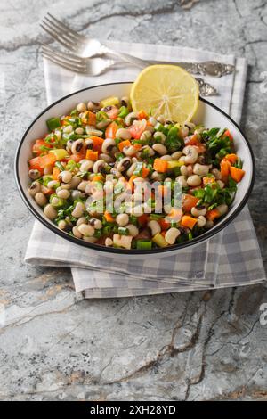 Salade de haricots aux yeux noirs avec carottes, oignons, tomates, basilic, persil habillé d'huile d'olive gros plan sur l'assiette sur la table. Vertical Banque D'Images