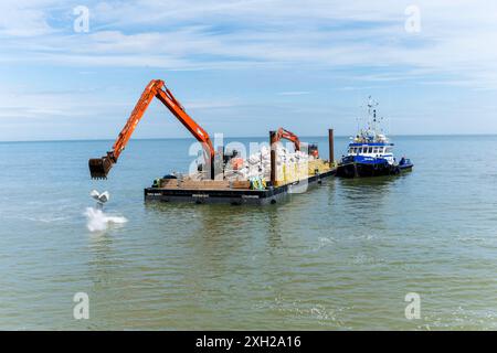 Travaux de protection contre l'érosion côtière avec des machines provenant d'une barge en mer, Cromer, Norfolk, Angleterre, Royaume-Uni, Europe Banque D'Images