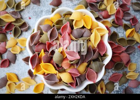 Fond de pâtes coloré. Vue de dessus des coquilles de pâtes cinq couleurs sur fond de pierre blanche. Pâtes au curcuma, aux épinards, à la betterave et à la carotte noire. Banque D'Images