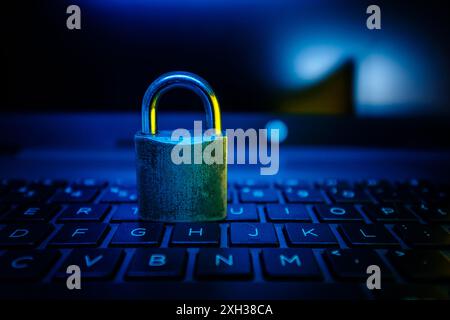 Un cadenas argenté repose sur un clavier d'ordinateur portable, éclairé par une lumière bleue. Banque D'Images