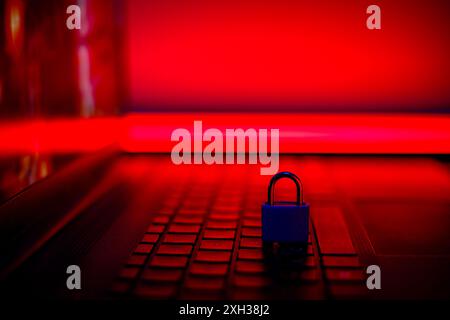 Un cadenas repose sur un clavier d'ordinateur portable, éclairé par une lumière rouge. Banque D'Images