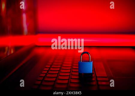 Un cadenas bleu repose sur un clavier d'ordinateur portable, avec une lumière rouge brillante de l'arrière-plan. Banque D'Images