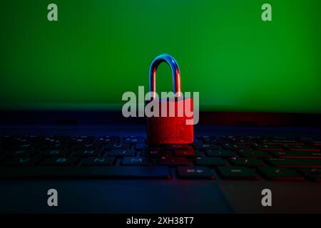 Un cadenas rouge se trouve sur un clavier d'ordinateur portable devant un écran vert. Banque D'Images