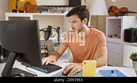 Un jeune homme hispanique avec une barbe travaille dans un studio de musique, axé sur le réglage du matériel. Banque D'Images