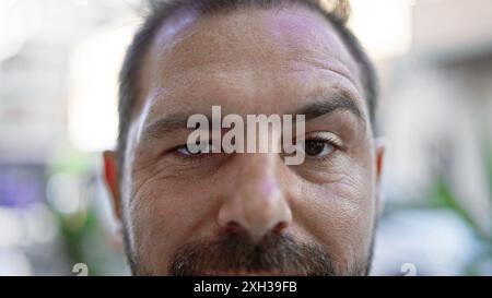 Portrait en gros plan d'un homme hispanique mature aux cheveux gris, montrant des yeux introspectifs et une rue urbaine dans le fond flou. Banque D'Images