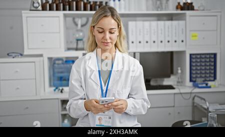 Une femme professionnelle en blouse de laboratoire utilise un smartphone dans un laboratoire moderne, représentant la technologie dans les soins de santé. Banque D'Images