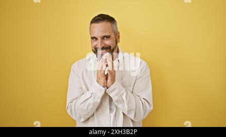 Un homme hispanique mûr joyeux avec une barbe grise souriant sur un fond jaune vif Banque D'Images