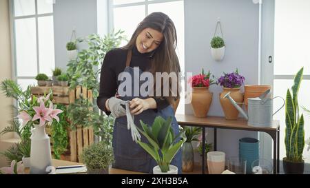 Une femme souriante portant un tablier met des gants au milieu de fleurs vibrantes dans un magasin de plantes d'intérieur. Banque D'Images