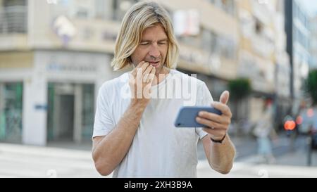 Homme concerné avec de longs cheveux blonds à l'aide d'un smartphone sur la rue de la ville Banque D'Images