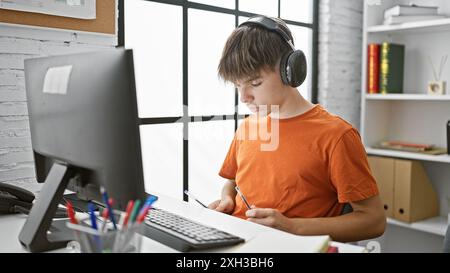 Un jeune adolescent blond étudie attentivement à son ordinateur dans une salle de classe moderne et lumineuse. Banque D'Images