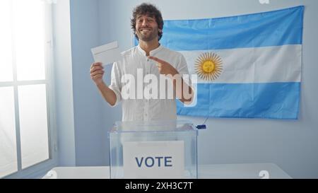 Jeune homme votant dans un collège électoral en argentine tenant un bulletin de vote et debout près d'une urne avec un drapeau argentin en arrière-plan Banque D'Images