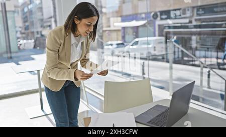 Une femme hispanique professionnelle examine des documents dans un bureau moderne avec des vues urbaines Banque D'Images