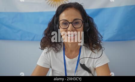 Femme souriante tout en portant un casque et assise devant un drapeau argentin lors d'un événement électoral intérieur. Banque D'Images