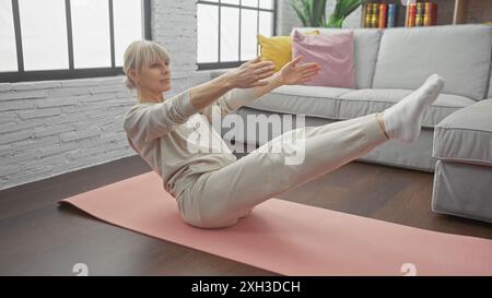 Femme mature pratique le yoga à l'intérieur de son salon d'appartement moderne, concept de santé et de remise en forme Banque D'Images
