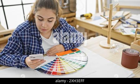 Une jeune femme examine des échantillons de couleur dans un atelier de menuiserie entouré de divers outils de menuiserie. Banque D'Images