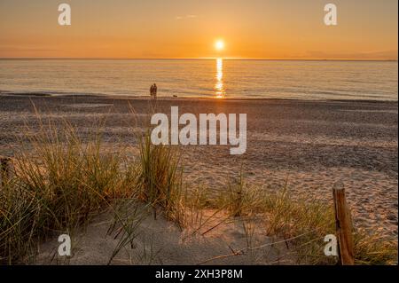 Un couple sur la plage au coucher du soleil et les dunes avec une clôture en fil de fer au premier plan, Skagen, Danemark, 30 mai 2024 Banque D'Images