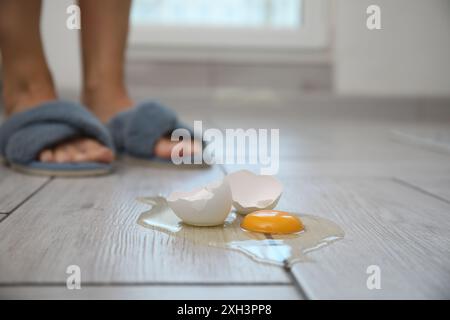 Femme près de l'oeuf cru cassé sur plancher en bois gris à l'intérieur, foyer sélectif. Espace pour le texte Banque D'Images