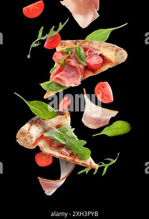 Tranches de pizza savoureuse et ingrédients dans l'air sur fond noir Banque D'Images