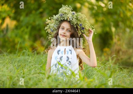 Jolie petite fille portant une couronne faite de belles fleurs dans le champ Banque D'Images