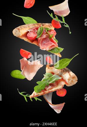 Tranches de pizza savoureuse et ingrédients dans l'air sur fond noir Banque D'Images