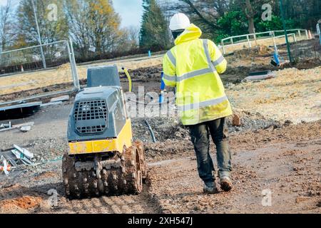 Rouleau de tranchée avec commande à distance actionné par un travailleur au sol pour compacter le sol sur le nouveau chantier de construction de logements. Rester à l'écart de la plante en mouvement Banque D'Images
