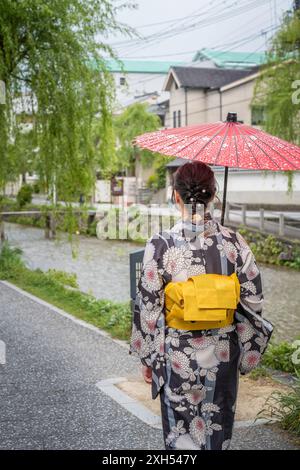 Femme japonaise portant un kimono traditionnel marchant avec un parapluie rouge dans la rue. Kyoto, Japon. Banque D'Images