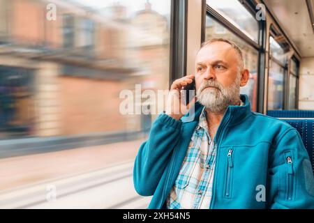 portrait d'un homme barbu dans une veste bleue parlant au téléphone dans un bus ou un tram. Concept de style de vie Banque D'Images