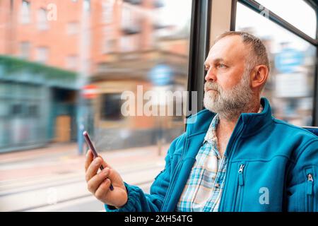 portrait d'un homme barbu dans une veste bleue parlant au téléphone dans un bus ou un tram. Concept de style de vie Banque D'Images