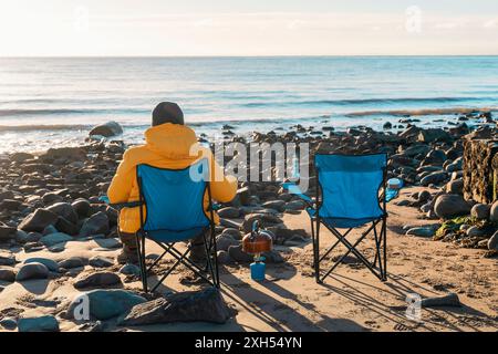 Deux personnes sur des chaises de plage ensemble sur la plage d'hiver, faire du thé chaud, du café le jour du ciel bleu ensoleillé et la mer en arrière-plan. Hiver froid britannique. La vie Banque D'Images