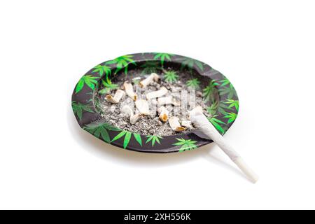 Cigarette commune de marijuana sur un cendrier sale avec motif de feuilles de cannabis, plat isolé sur blanc Banque D'Images