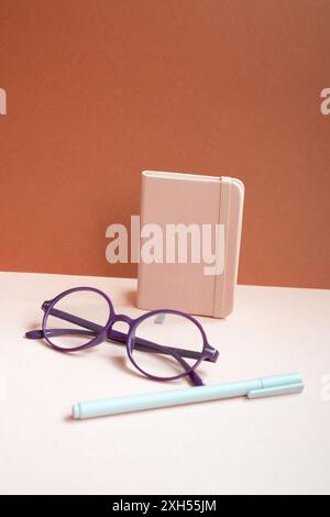 Carnet d'agenda, stylo, lunettes sur le bureau rose. fond rouge Banque D'Images