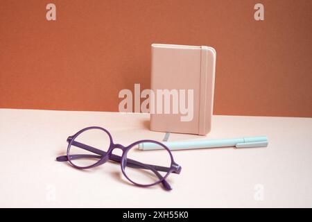 Carnet d'agenda, stylo, lunettes sur le bureau rose. fond rouge Banque D'Images
