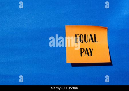Message d'égalité salariale écrit sur du papier orange avec fond bleu. Symbole conceptuel de l'égalité salariale. Copier l'espace. Banque D'Images
