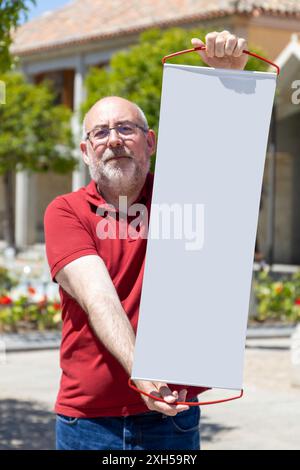 Un homme en chemise rouge tient une grande bannière blanche. Concept de positivité et d'excitation, comme l'homme tient une toile vierge qui pourrait être remplie avec Banque D'Images