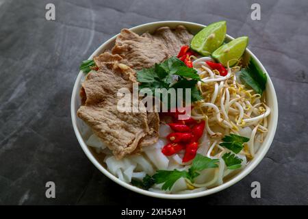 Un bol soupe traditionnelle Pho Bo avec bœuf, nouilles de riz, gingembre, citron vert, piment dans un bol. Gros plan. Cuisine vietnamienne servie sur fond noir Banque D'Images