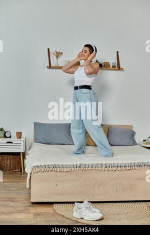 Jeune femme aux cheveux courts se tient au sommet du lit dans une chambre confortable, incarnant la paix et la tranquillité. Banque D'Images