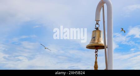 Cloche de navire sur un mât blanc contre un ciel bleu avec mouettes, voyage en mer, vacances à l'océan Banque D'Images