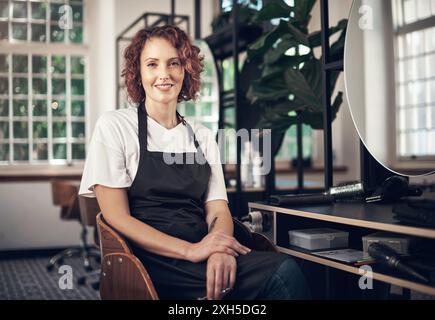 Portrait, femme et coiffeur en salon, chaise et petite entreprise pour les soins capillaires, employé et tablier. Démarrage, entretien et personne avec les outils pour Banque D'Images